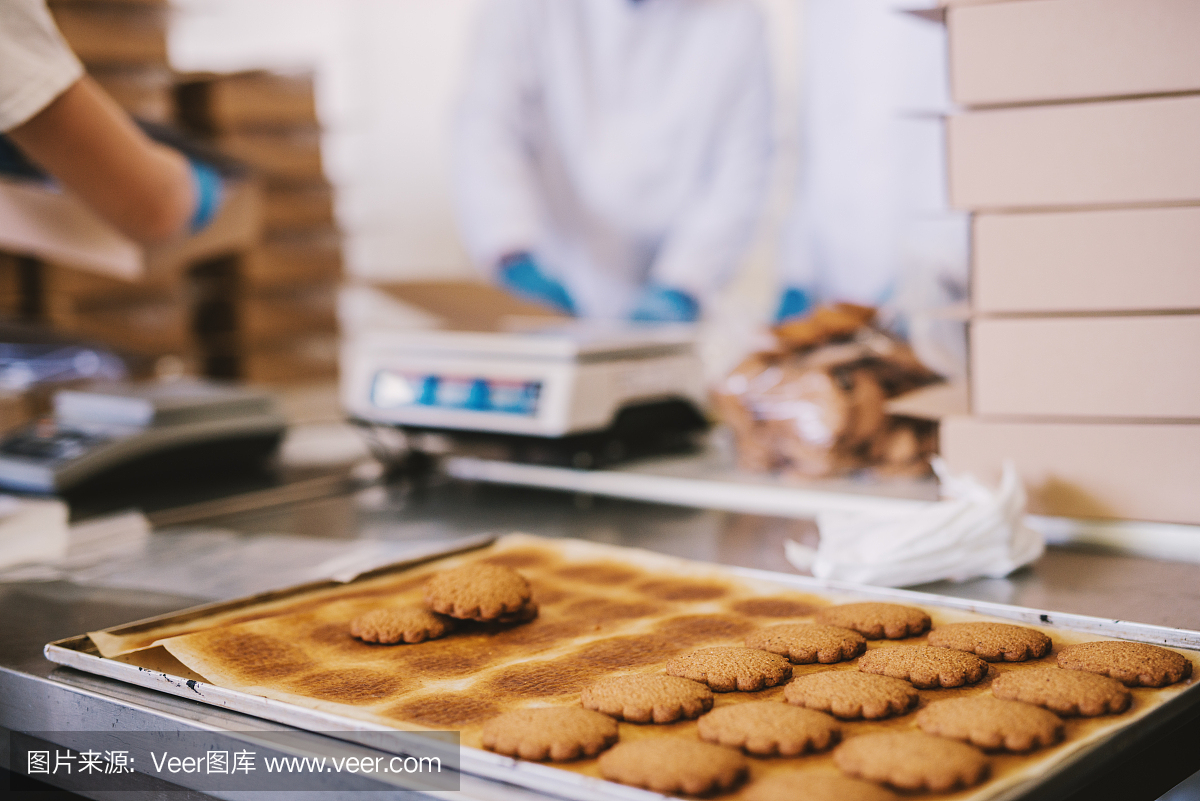 在食品工廠(chǎng)里裝滿(mǎn)了新鮮出爐的餅干。背景是兩名男性員工穿著無(wú)菌衣服包裝餅干的模糊圖片。